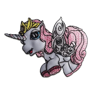 Könnte beinhalten: Gestickter Aufnäher eines skurrilen Einhorns mit silbernem Horn, goldener Krone und rosa Mähne und Schweif. Das Einhorn hat blaue Augen und dekorative Flügel mit schwarzen Details. Der Aufnäher befindet sich auf weißem Hintergrund.