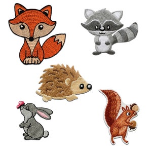 May include: Embroidered patches of woodland creatures: a fox, raccoon, hedgehog, rabbit, and squirrel. The fox is orange and tan, the raccoon is grey, the hedgehog is brown, the rabbit is grey, and the squirrel is brown.