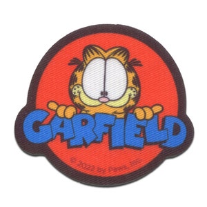 Puede incluir: Un parche circular con Garfield el gato con la palabra "GARFIELD" en letras azules. El parche tiene un fondo rojo con un borde marrón. Garfield es naranja y amarillo con una expresión sonriente.