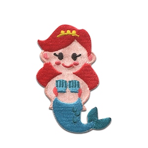 Può includere: Una sirena dai capelli rossi con una coda blu e un reggiseno a conchiglia rosa. Indossa una corona gialla sulla testa e ha un viso sorridente.