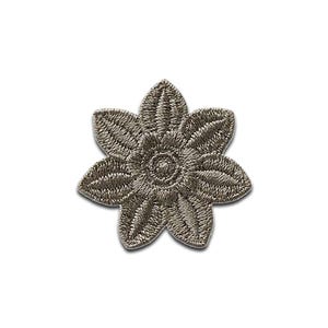 May include: A taupe-colored embroidered flower patch featuring a six-petaled design with a circular center. The embroidery consists of dense, radiating thread patterns that create a textured, raised surface across the entire floral shape.