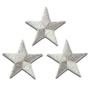 May include: Three silver embroidered stars, each with five points, are arranged in a triangular pattern. The stars are approximately 2.5 cm in diameter.