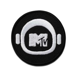 Può includere: Toppa rotonda nera con logo MTV bianco. Il logo è all'interno di un contorno bianco di cuffie. La toppa è probabilmente per abbigliamento o accessori ed è un simbolo popolare della musica e della cultura pop.