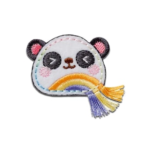 Op de afbeelding: Een witte pandabeer met zwarte ogen en oren, die een regenboog vasthoudt met een gele kwast. De panda glimlacht en heeft roze wangen.