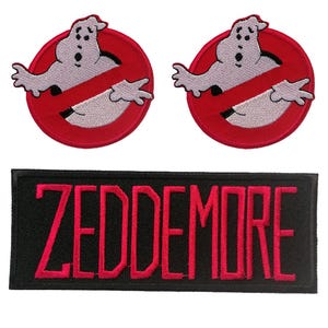Op de afbeelding: Twee ronde geborduurde patches met een wit spookfiguur in een rode cirkel met een rode diagonale streep, en één rechthoekige zwarte patch met de naam ZEDDEMORE geborduurd in dikke rode hoofdletters.