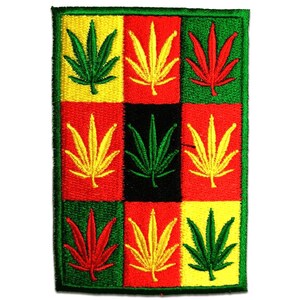 Könnte beinhalten: Gestickter Aufnäher mit einem Rastermuster. Es zeigt neun Cannabisblätter in Grün, Gelb und Rot, vor einem schwarzen, gelben und roten Hintergrund. Der Aufnäher hat einen grünen Rand.