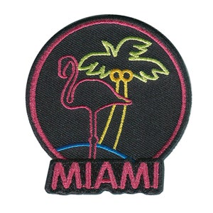 May include: Pink flamingo and palm tree neon sign with the word "MIAMI" in pink lettering on a black background.