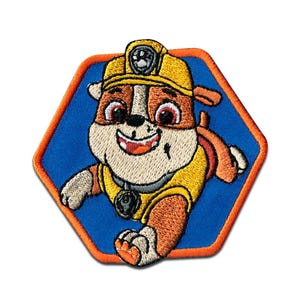 Op de afbeelding: Geborduurde patch met een cartoonhond in een geel uniform en helm, tegen een blauwe zeshoekige achtergrond met een oranje rand. De hond heeft bruine en witte vacht, een lachende uitdrukking en een badge.
