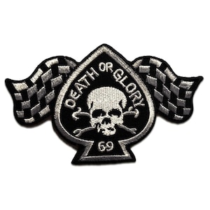 Könnte beinhalten: Schwarz-weißer, gestickter Aufnäher mit einem Totenkopf und gekreuzten Knochen in einer Pikform. Die Worte "DEATH OR GLORY" sind um den Totenkopf herum angeordnet. Schachbrettflaggen erstrecken sich von den Seiten, und die Zahl "69" befindet sich unten.