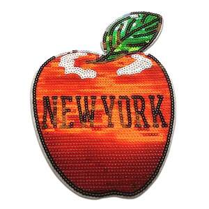 Può includere: Una toppa a forma di mela con paillettes con la scritta "NEW YORK". La mela è principalmente rossa e arancione, con una foglia verde e dettagli bianchi. La toppa è probabilmente per abbigliamento o accessori.
