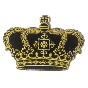 Puede incluir: Un parche de corona bordado en oro sobre un fondo negro. La corona tiene una cruz en la parte superior y detalles intrincados.