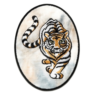 May include: An embroidered patch of a tiger with orange and black stripes, walking towards the viewer with its mouth closed. The tiger is on a white oval background with a black border.