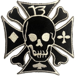 Könnte beinhalten: Schwarz-weißer, gestickter Aufnäher mit einem Totenkopf mit gekreuzten Knochen in der Mitte eines kreuzförmigen Designs. Die Zahl "13" befindet sich oben. Das Design enthält Karo-, Kreuz- und Pik-Symbole.