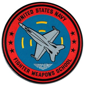 Può includere: Toppa rotonda ricamata con un jet da combattimento grigio su sfondo blu, circondata da un bordo rosso. Il testo recita "UNITED STATES NAVY FIGHTER WEAPONS SCHOOL". Include il logo "TOP GUN MAVERICK" e stelle.