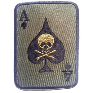 Op de afbeelding: Een rechthoekige patch met het ontwerp van de Aas van Schoppen kaart. De schoppen is marineblauw met een gouden schedel en gekruiste botten. De achtergrond is olijfgroen met een marineblauwe rand. De symbolen en letters zijn marineblauw en goud.