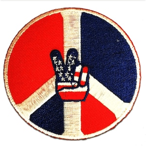 Op de afbeelding: Een ronde vredesduif-patch met een rood, wit en blauw Amerikaans vlagontwerp. Het vredesduif-symbool is gemaakt van wit garen en de vlag is geborduurd op het vredesduif-symbool.