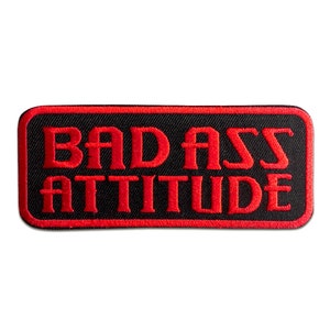 May include: A black rectangular patch with a red border. The text "BAD ASS ATTITUDE" is embroidered in red.