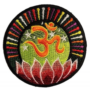 Puede incluir: Parche bordado redondo con un símbolo Om naranja sobre un fondo verde, rodeado por un borde negro. El diseño incluye una flor de loto roja y blanca en la parte inferior y rayas verticales coloridas alrededor del borde. También se incluyen tres estrellas blancas.