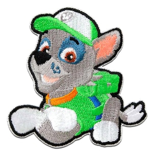 Op de afbeelding: Geborduurde patch met een cartoonhond in grijstinten, groen en oranje. De hond draagt een groene pet en rugzak. De patch heeft een witte rand en is bedoeld voor toepassing op kleding of accessoires.