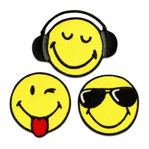 Op de afbeelding: Drie ronde geborduurde patches met gele smiley-gezichten. Eén gezicht draagt een zwarte koptelefoon, één knipoogt met de tong uitgestoken in rood, en één draagt een zwarte zonnebril. Elke patch heeft een dikke zwarte gestikte rand.