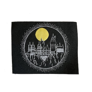 May include: A black fabric patch with a white embroidered image of Hogwarts castle, a yellow moon, and a circle of white dots.