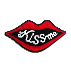 Könnte beinhalten: Rote gestickte Lippen mit dem Text "Kiss Me" in weißen Buchstaben auf schwarzem Hintergrund.