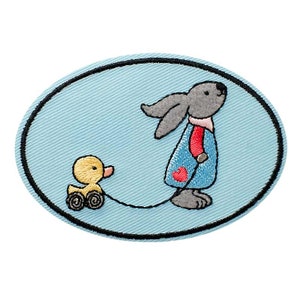 Könnte beinhalten: Ein gestickter Bügel-Patch mit einem grauen Hasen in einem blauen Kleid mit einem roten Herzen, der einen gelben Enten auf Rädern zieht.