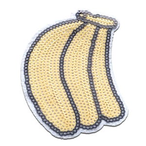 Könnte beinhalten: Ein gelber Pailletten-Bananen-Aufnäher mit grauem Rand und weißer Rückseite. Die Banane besteht aus kleinen, glänzenden Pailletten und hat eine gebogene Form. Der Aufnäher ist wahrscheinlich für Kleidung oder Accessoires.