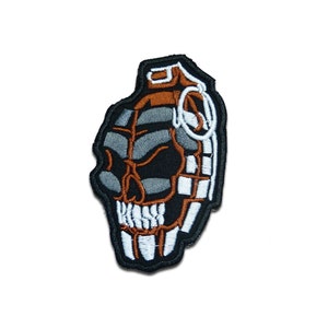 May include: A black and white embroidered patch of a skull shaped like a grenade. The grenade is brown and white with a black fuse.
