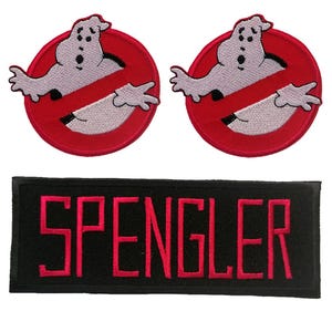 Op de afbeelding: Twee ronde geborduurde patches met een wit spookfiguur in een rode cirkel met een rode diagonale streep, en één rechthoekige zwarte patch met de naam SPENGLER geborduurd in dikke rode hoofdletters.