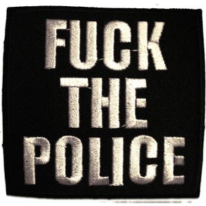 May include: A black square patch featuring the embroidered words "FUCK THE POLICE" in white, capital letters. The text has a bold, raised appearance against the black background.