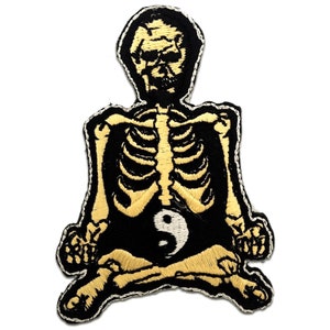 Puede incluir: Parche bordado con un esqueleto amarillo sentado en posición de meditación con un símbolo yin yang en el estómago. El fondo es negro.