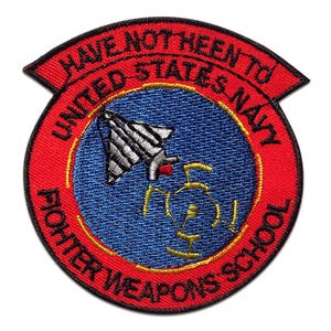 Può includere: Toppa ricamata circolare con bordo e testo rossi. La toppa presenta il testo "HAVE NOT BEEN TO UNITED STATES NAVY FIGHTER WEAPONS SCHOOL". Il centro ha uno sfondo blu con un aereo stilizzato e dettagli gialli.