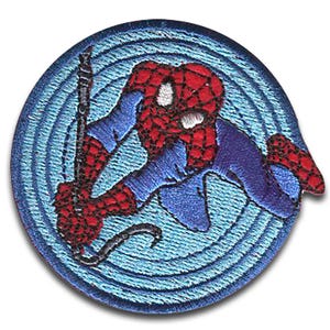 Op de afbeelding: Geborduurd embleem met Spider-Man in een dynamische pose. Het embleem toont de superheld in zijn iconische rood-blauwe pak, met witte ogen, tegen een lichtblauwe cirkelvormige achtergrond. Een zwarte weblijn is zichtbaar.