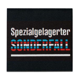 Könnte beinhalten: Schwarzer Stoff-Patch mit weißem Text, der "Spezialgelagerter Sonderfall" in einer rot-weiß-blauen gestreiften Schriftart lautet.
