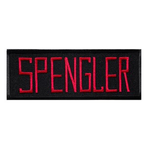 Könnte beinhalten: Ein rechteckiger, schwarzer Aufnäher mit dem Namen "SPENGLER", der in leuchtend roter Farbe gestickt ist. Die Buchstaben sind blockartig und heben sich deutlich vom dunklen Hintergrund ab. Der Aufnäher ist zum Aufnähen auf Kleidung oder Accessoires gedacht.