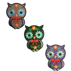 Könnte beinhalten: Drei gestickte Bügeleisen-Aufnäher mit Eulen und floralen Details. Die Eulen sind braun, grün und lila. Jede Eule hat eine rote Schleife und ein florales Design um den Kopf.