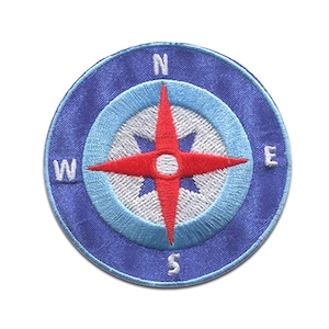 Könnte beinhalten: Ein runder, gestickter Aufnäher mit einem Kompass-Design. Der Aufnäher hat einen blauen Rand mit den Buchstaben N, E, S und W. Im Inneren befindet sich eine rote Windrose auf einem weißen und hellblauen Hintergrund.