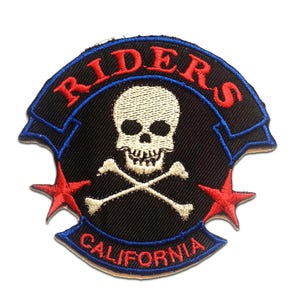 Könnte beinhalten: Gestickter Aufnäher mit Totenkopf und gekreuzten Knochen. Der Aufnäher hat einen schwarzen Hintergrund mit roten Sternen und den Text "RIDERS" und "CALIFORNIA" in Rot und Blau.