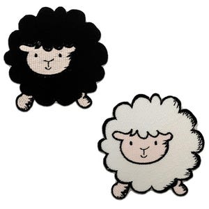 Pode incluir: Dois patches de ovelhas bordadas. Um é uma ovelha preta com rosto branco e detalhes rosa. O outro é uma ovelha branca com rosto rosa e detalhes rosa. Ambos os patches têm uma aparência fofa, semelhante a uma nuvem.
