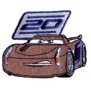 Può includere: Macchina da corsa di cartoni animati marrone e nera con un numero 95 blu e argento sul tetto. L'auto ha un parabrezza nero e fari blu. L'auto è ricamata.