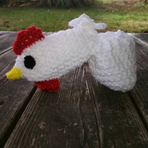 Op de afbeelding: Witte gehaakte babyschoentjes in de vorm van een kip met rode en gele accenten.