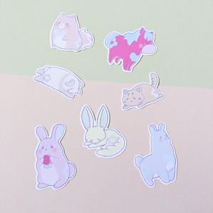 Pode incluir: Um conjunto de sete adesivos de animais em tons pastel. Os adesivos apresentam um cavalo rosa, uma lhama azul claro, um coelho verde claro, um coelho amarelo claro, um gato castanho claro, um cão branco e rosa e um coelho branco e rosa.