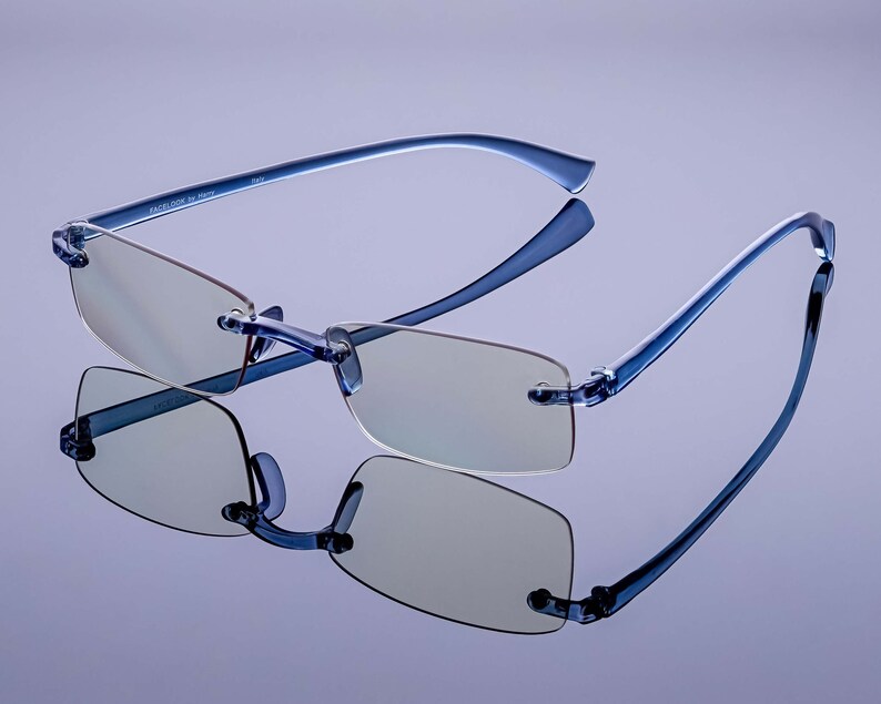 Puede incluir: Gafas sin montura azules con un marco azul claro y lentes transparentes. Las gafas est&aacute;n sobre una superficie de color p&uacute;rpura claro.