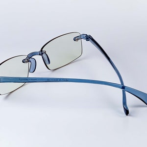 Puede incluir: Gafas de montura de pl&aacute;stico azul con lentes transparentes. Las patillas de las gafas est&aacute;n dobladas y el texto "AE2111 C2 11011 14E" est&aacute; impreso en la patilla derecha.
