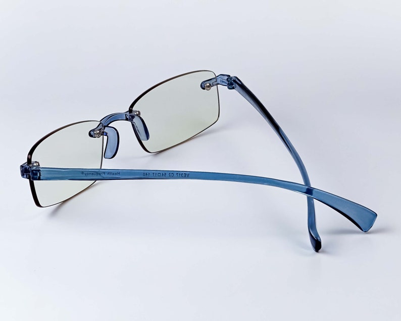 Puede incluir: Gafas de montura de pl&aacute;stico azul con lentes transparentes. Las patillas de las gafas est&aacute;n dobladas y el texto "AE2111 C2 11011 14E" est&aacute; impreso en la patilla derecha.