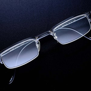 May include: Clear plastic framed glasses with the text "HARRY  Leather Italy" on the left frame and "MR.MO62 47-21-140" on the right frame.