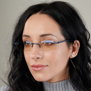 Puede incluir: Una mujer con gafas sin montura con un marco azul y lentes &aacute;mbar. Las gafas tienen una forma rectangular.