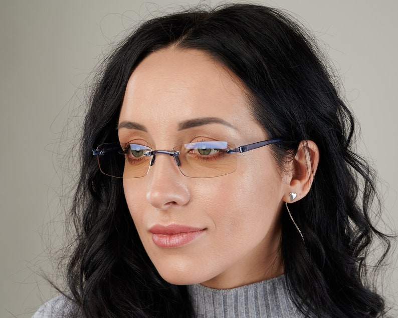 Puede incluir: Una mujer con gafas sin montura con un marco azul y lentes &aacute;mbar. Las gafas tienen una forma rectangular.