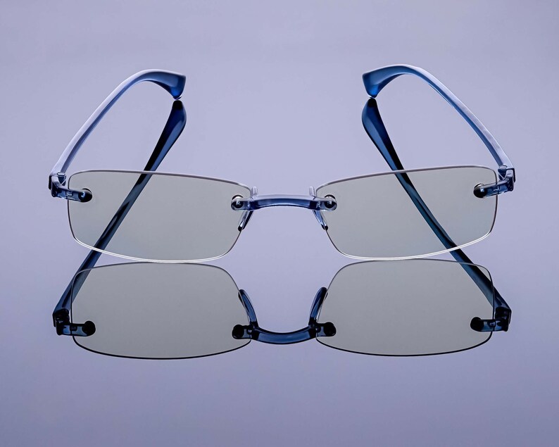 Puede incluir: Un par de gafas azules sin montura con lentes gris claro. Las gafas se reflejan en una superficie de espejo.